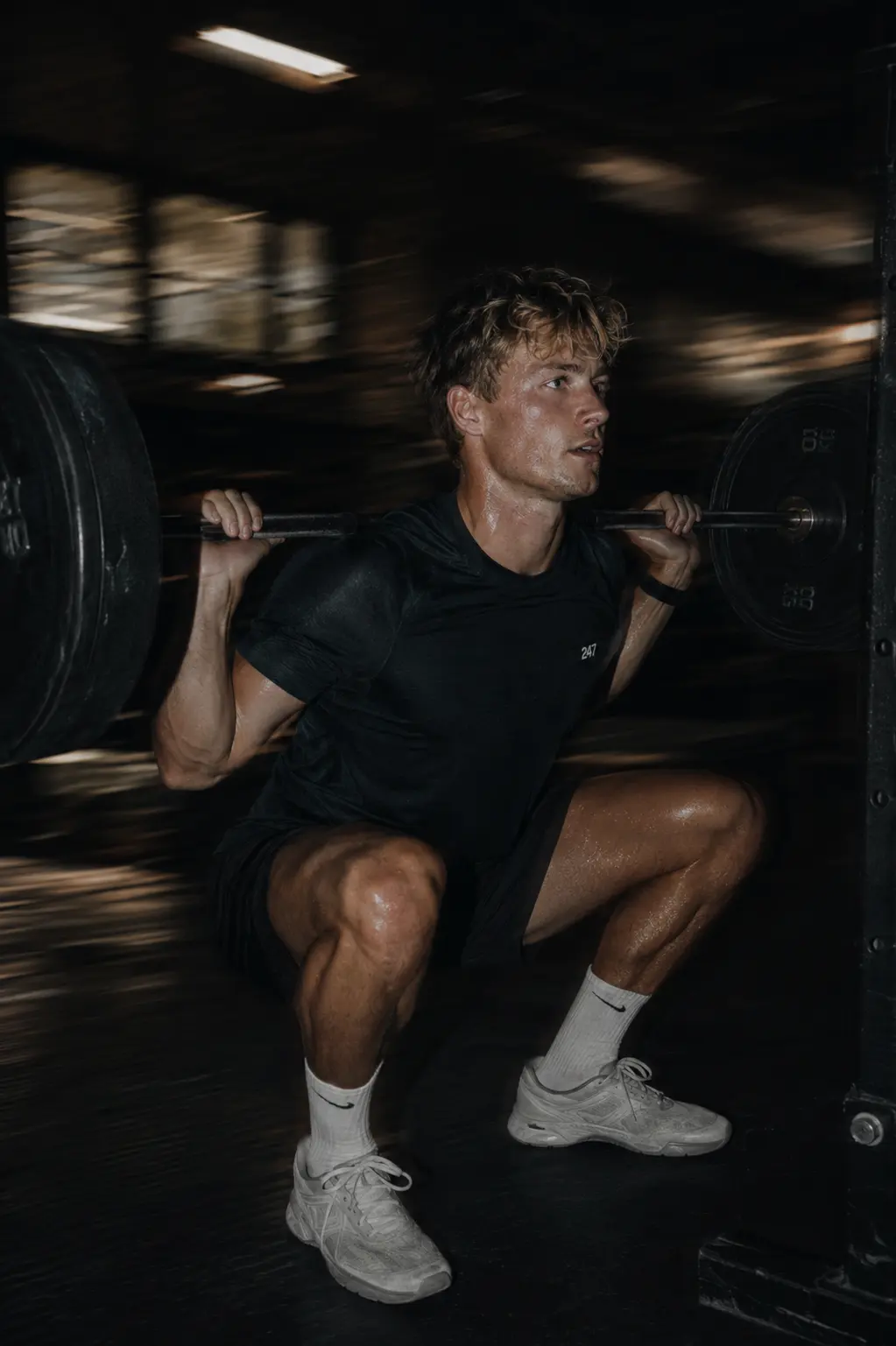 A lifter under a loaded barbell in a squat rack